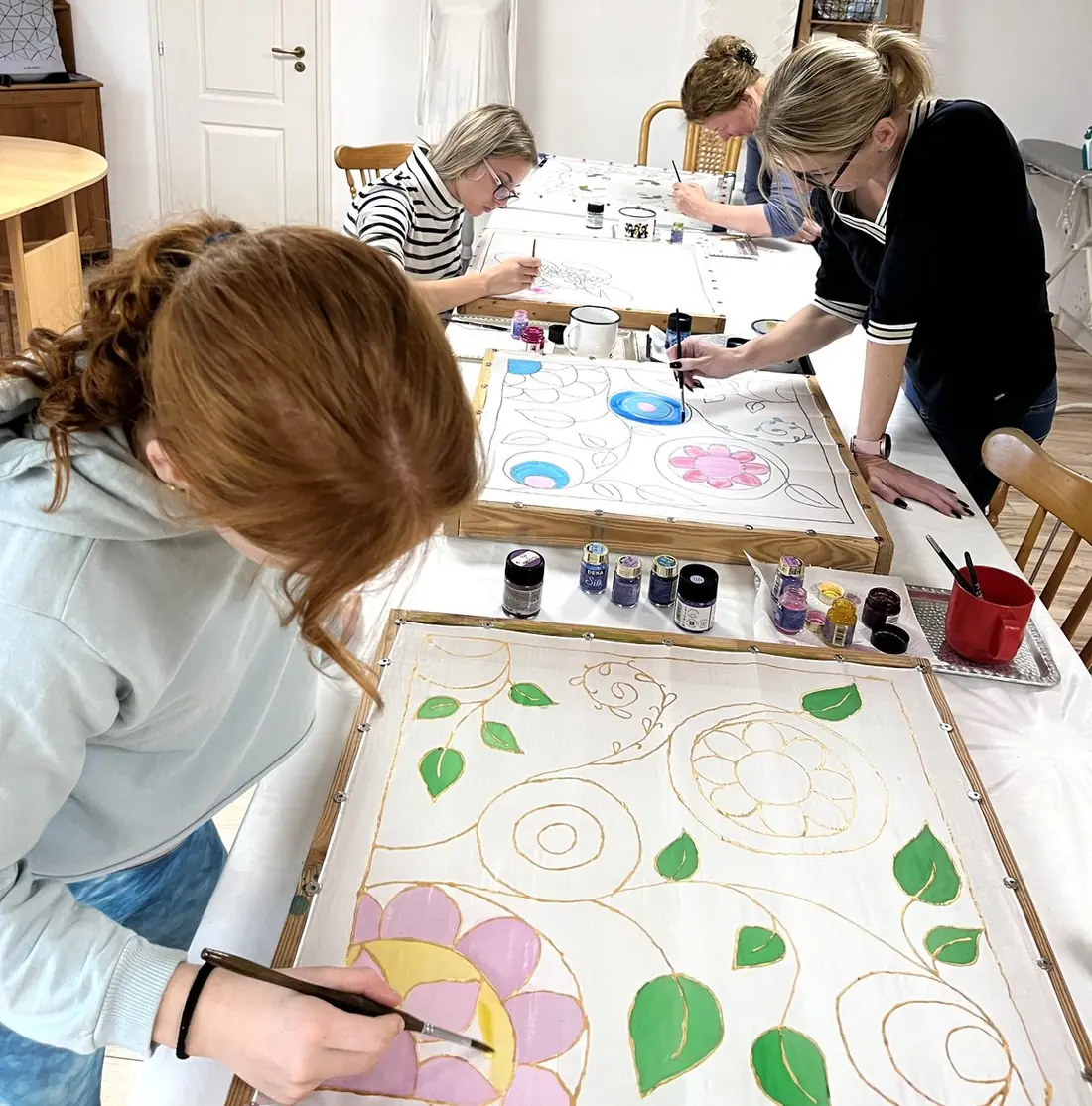 Előre megkontúrozott virágmintás selyemkendőt fest egy résztvevő a workshopon